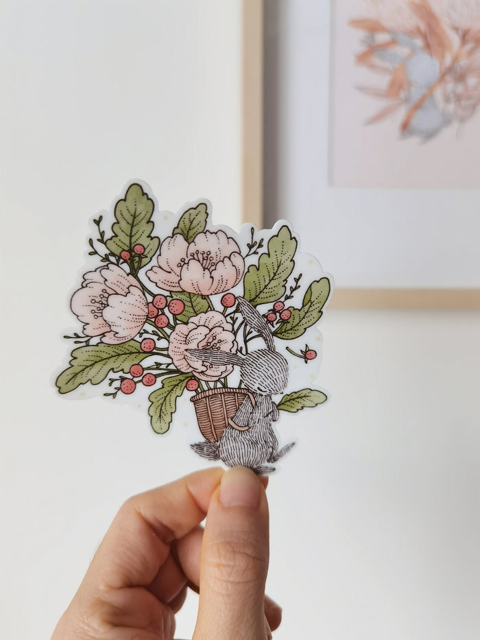 Waterproof sticker featuring rabbit carries a basket full of blooms. Add a touch of floral charm to laptops, journals, sketchbooks, and any surface.