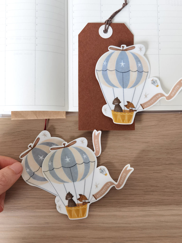 Waterproof sticker featuring fox and bear soaring in a hot air balloon. Add a touch of wanderlust to laptops, journals, sketchbooks, and any surface.