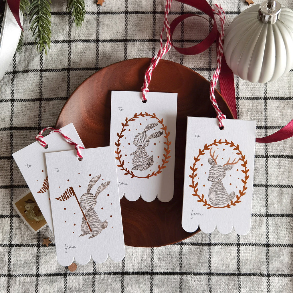 Rectangular Christmas gift tags with illustrated rabbit and reindeer wreaths in shimmering copper foil on sturdy cardstock. Scalloped edge on one side. Ideal for holiday gifting.