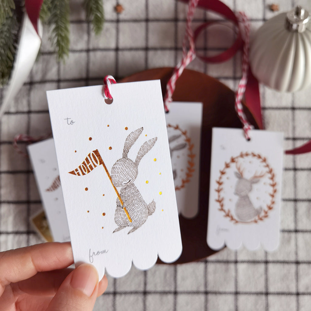 Rectangular Christmas gift tags with illustrated rabbit and reindeer wreaths in shimmering copper foil on sturdy cardstock. Scalloped edge on one side. Ideal for holiday gifting.