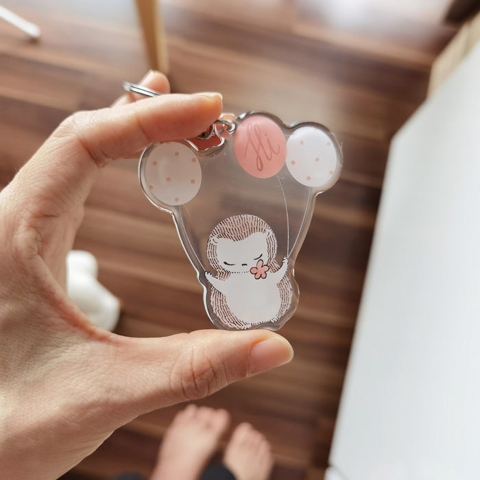 Charming acrylic keycharm featuring a hedgehog and party balloons, adds whimsical touch to bags and keys. A stylish accessory.
