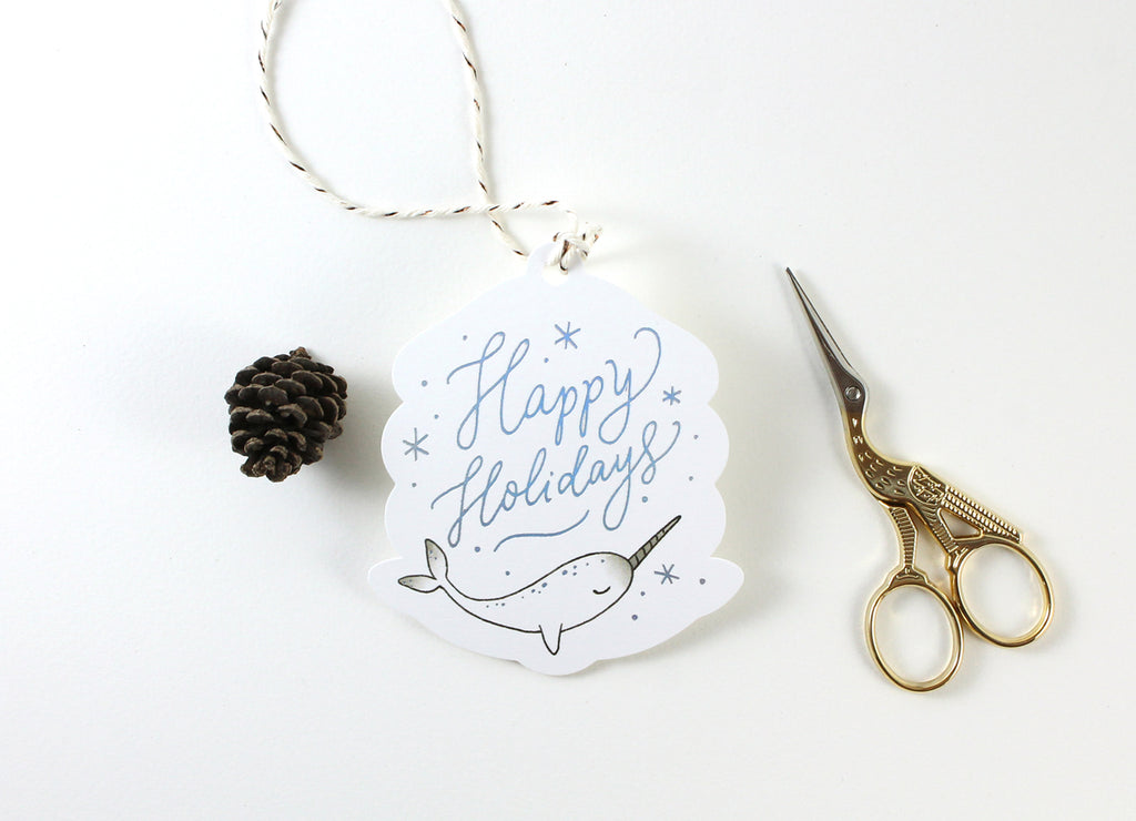 Holographic Foil Christmas Holiday Gift Tags - Happy Holidays Narwhal gift tags - showcasing 'Happy Holidays' hand-lettered printed in holographic foil, a whimsical illustrated narwhal, uniquely custom die-cut shape, adorned with cotton twine.