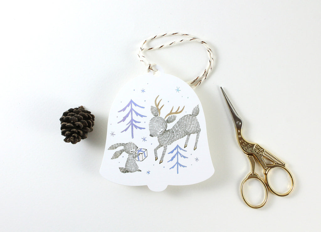 Holographic Foil Christmas Holiday Gift Tags - Rabbit, Reindeer & Christmas Gift - winter forest trees elegantly printed in holographic foil, whimsical illustration of rabbit presenting a gift to a reindeer, custom die-cut in the shape of a bell, adorned with cotton twine.
