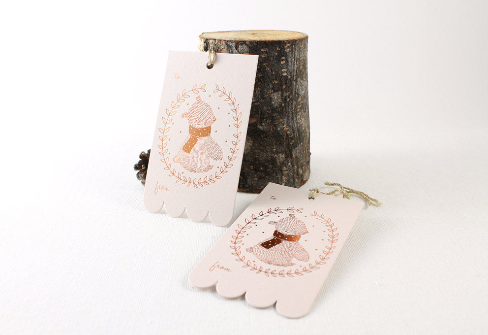Rectangular Christmas gift tag with illustrated winter bear and festive wreath design in shimmering copper foil on blush pink cardstock. Scalloped edge on one side. Ideal for holiday gifting and Christmas presents.