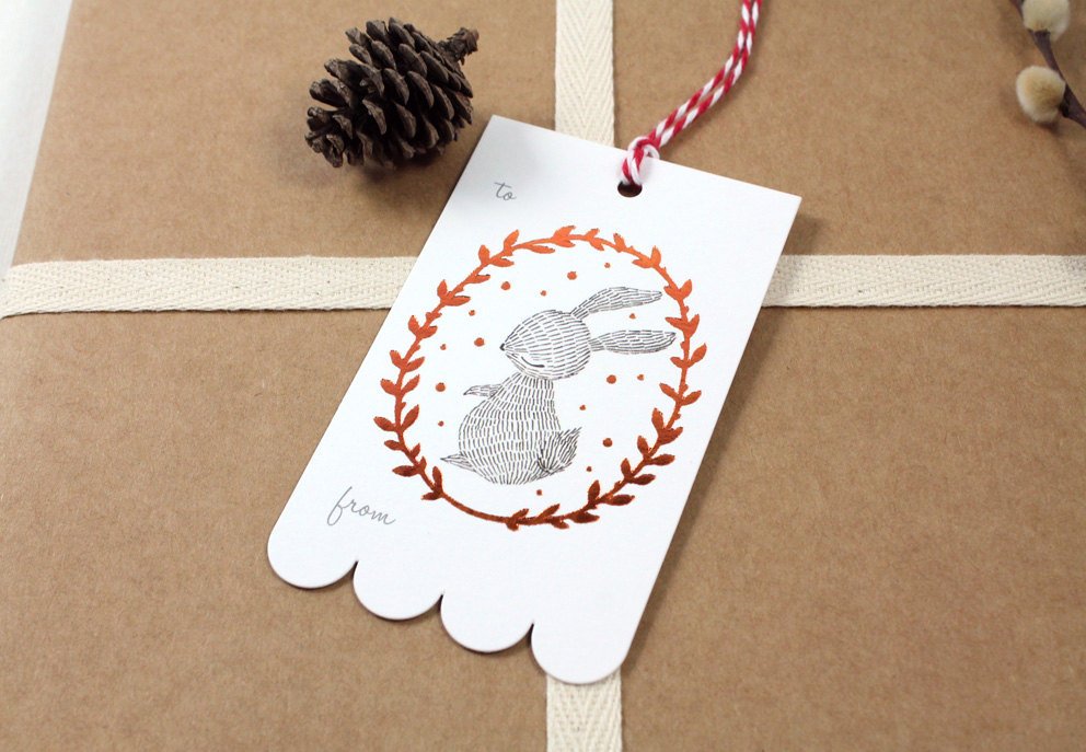 Rectangular Christmas gift tag with illustrated rabbit in shimmering copper foil wreath on sturdy cardstock. Scalloped edge on one side. Ideal for holiday gifting.