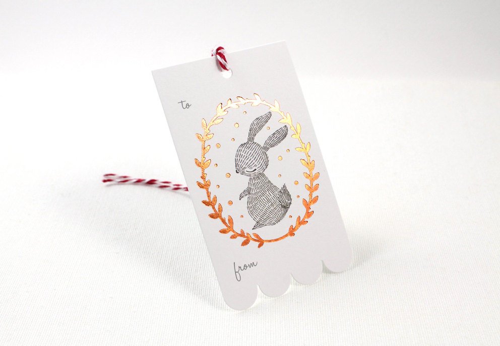 Rectangular Christmas gift tag with illustrated rabbit in shimmering copper foil wreath on sturdy cardstock. Scalloped edge on one side. Ideal for holiday gifting.