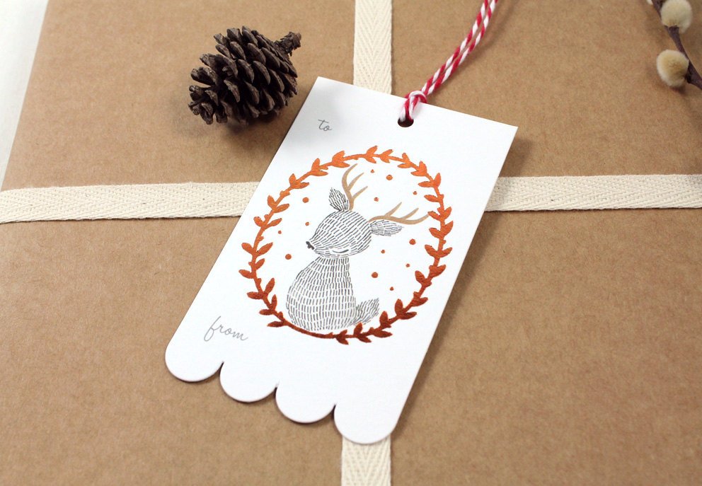 Rectangular Christmas gift tag with illustrated reindeer in shimmering copper foil wreath on sturdy cardstock. Scalloped edge on one side. Ideal for holiday gifting.
