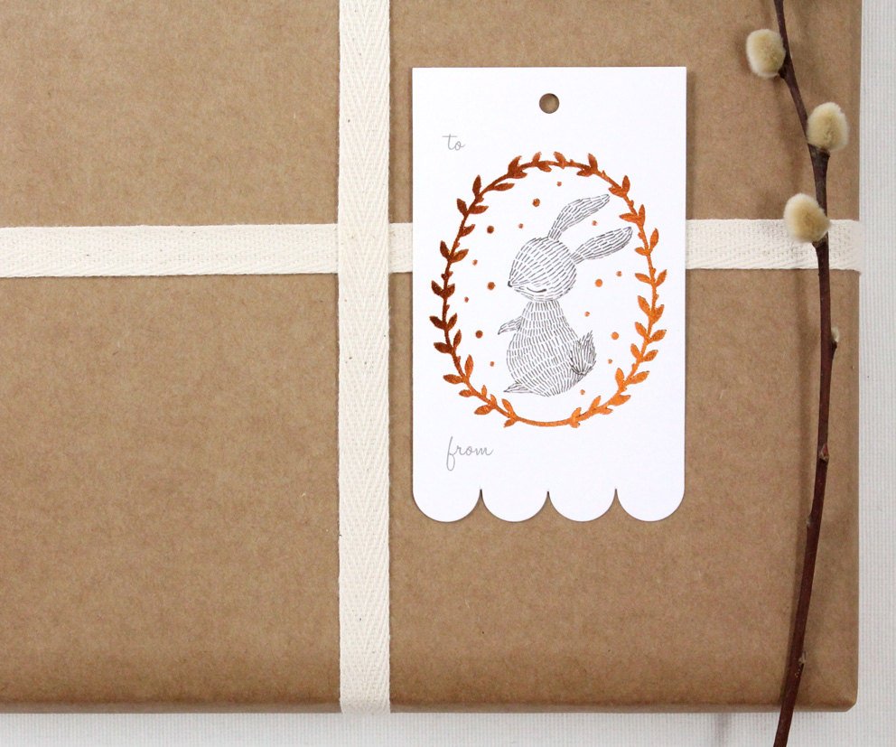 Rectangular Christmas gift tag with illustrated rabbit in shimmering copper foil wreath on sturdy cardstock. Scalloped edge on one side. Ideal for holiday gifting.